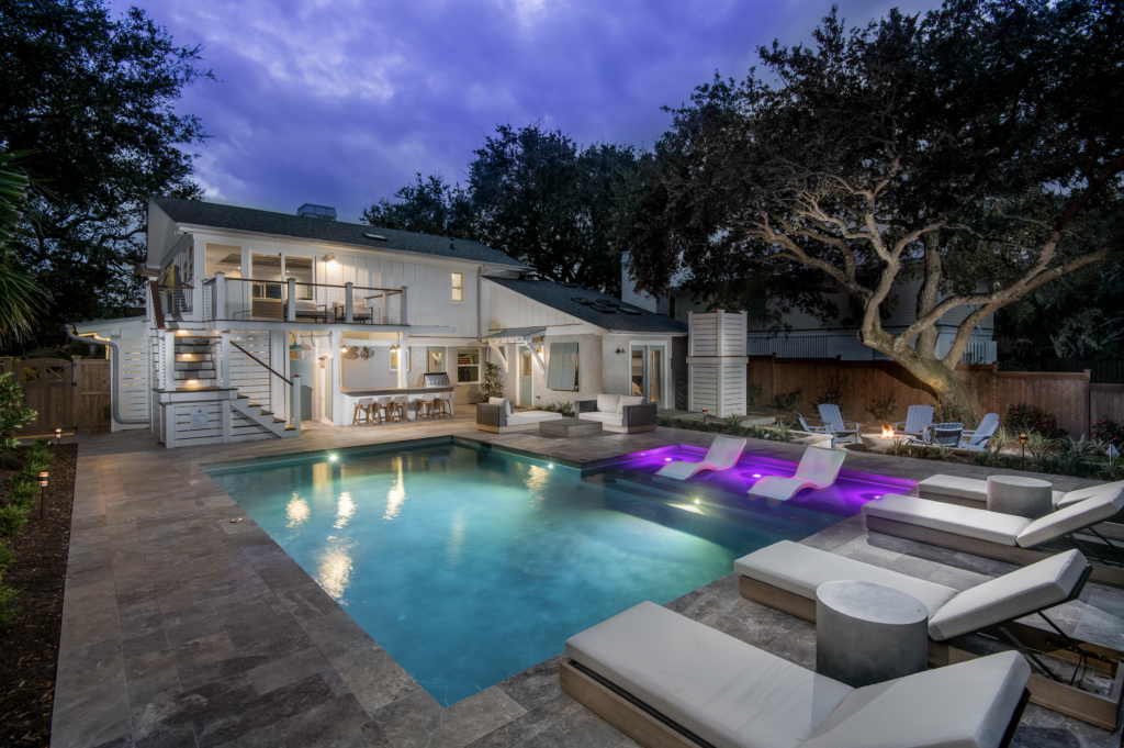 Backyard pool lit up at night with lounge chairs and tanning ledge feature