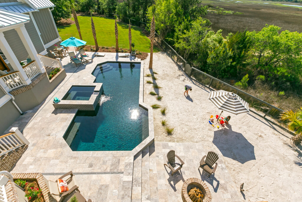 Aerial view of backyard with pool, lounge chairs and little girl and dad playing in beach sand